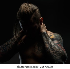 Portrait of a man with naked torso and tattooes. Dark and deep shadows. 