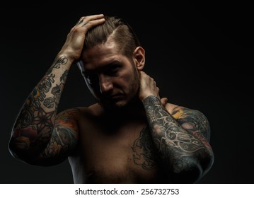 Portrait of a man with naked torso and tattooes. Dark and deep shadows. 