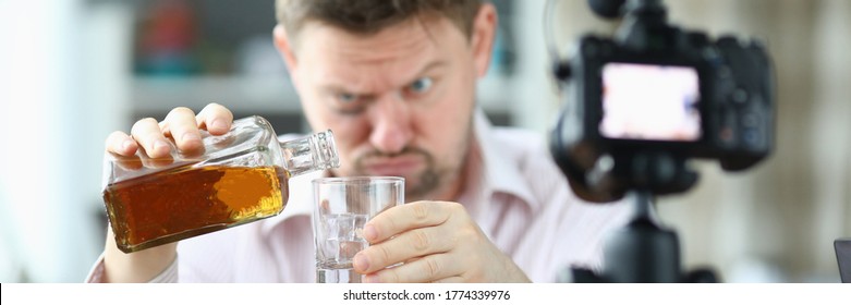 Porträt von Menschen, die Whiskey in Glas aus Flasche gießen. Guy sieht betrunken aus und filmt auf Videokamera. Entferne das Hemd und bläst unter den Augen. Produktion unter Kamera