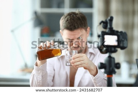 Portrait of man pouring whiskey into glass from bottle. Guy looking drunk and filming on videocamera. Unbutton shirt and bruise under eye. Production on camera Foto d'archivio © 