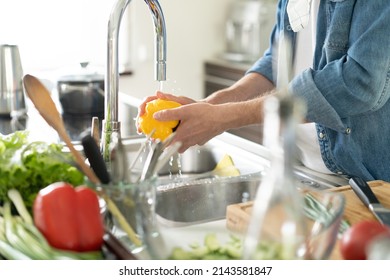 Portrait of man preparing wash fresh vegetables salad splashing in water on counter standing in the home kitchen - Powered by Shutterstock