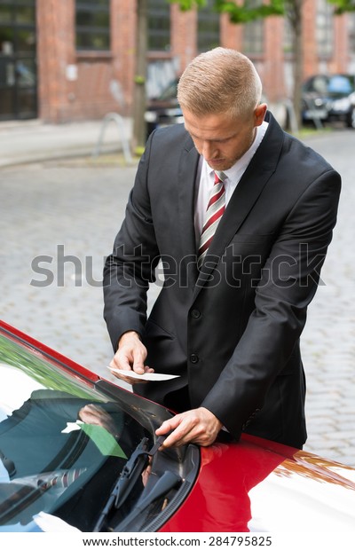 Portrait Of A Man Removing Parking Ticket On\
Car Windscreen