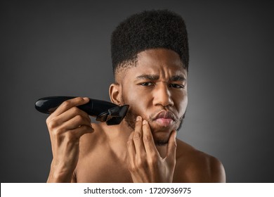 Portrait of man shaving his beard with electric shaver against dark grey background