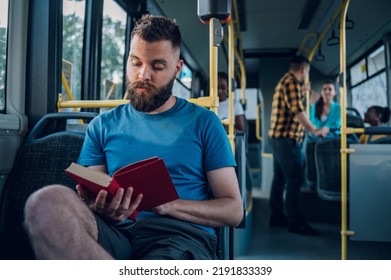 Portrait Of A Man Sitting In A Bus And Reading A Popular Fiction Book. Everyday Life And Commuting To Work By Public Transportation. Man Is Reading A Novel And Enjoying His Ride.