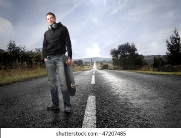 Portrait of a man standing on a countryside road with a skateboard in his hand - Powered by Shutterstock