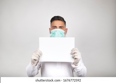 Portrait Of Man In Surgical Mask Holding A White Sign On White Background.