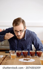 Portrait Of Man Tasting Freshly Brewed Coffee In Glass Cup, Using Spoon, Examining Coffee Taste And Flavour At Coffee Cupping Test For Barosta