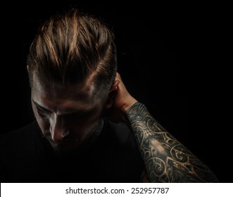Portrait of a man with  tattoos. Dark and deep shadows. Isolated on black.