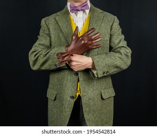 Portrait Of Man In Vintage Tweed Suit Pulling On Leather Gloves On Black Background. Concept Of Classic And Eccentric British Gentleman Stereotype. Retro Style And Vintage Fashion.