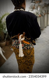 Portrait of a man walking with his back to the camera at a Javanese Indonesian wedding ceremony with a bridal keris behind his back, indonesian wedding