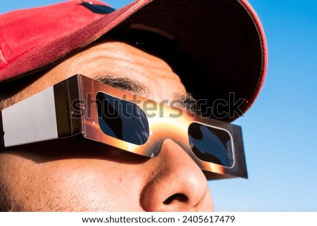 Portrait of man wearing cap and solar eclipse glasses, looking sun with blue sky at background 
