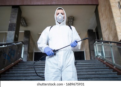 Portrait of man in white protection suit with sprayer tank ready for a fight against coronavirus. Disinfecting streets and public areas to stop spreading COVID-19.