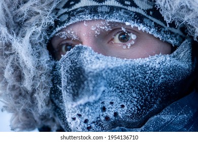 Portrait of a man in winter clothes and a mask. A traveler in the Arctic. Ice and snow on eyelashes, face and mask. Cold polar climate. Extreme travel and expeditions to the far North to the Arctic.