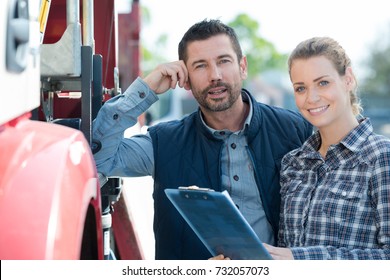 portrait of man and woman holding clipboard next to truck