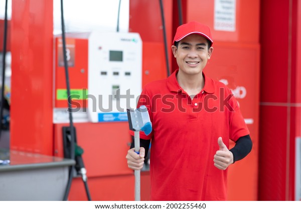 Portrait of Man worker in red uniform holding\
sponge clean windscreen of car while representing high quality\
service of gas fuel\
station