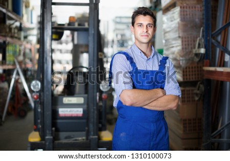 Portrait of man worker in uniform  standing near shelving in building workshop


