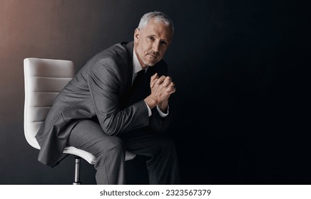 Portrait, manager or corporate with a business man sitting on a chair in studio against a dark background. Leadership, management and a senior male CEO in a professional suit for his executive career - Shutterstock ID 2323567379