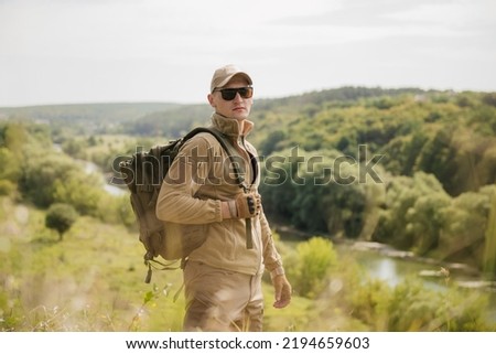 Portrait of masculine fisher hunter man with hatchet axe wearing tactical gear exploring the river outdoors landscape