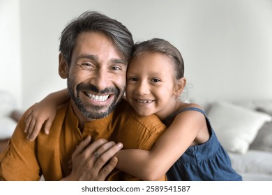 Portrait of mature 40s portuguese father and little 5s daughter hugging seated on sofa, exuding joy, connection and affection, close up photo. Warmth, closeness between daddy and child, family ties