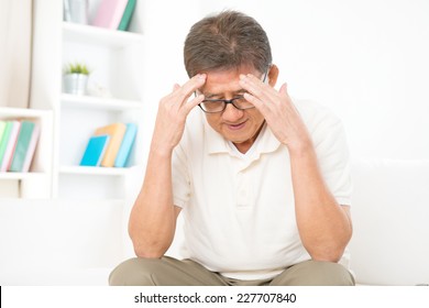 Portrait Of Mature Asian Man Having Headache, Sitting On Sofa At Home, Senior Retiree Indoors Living Lifestyle. 