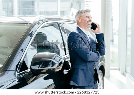 Portrait of mature attractive beard businessman wearing blue formal suit talking on smartphone while standing outside the car.