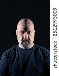 Portrait of a mature bald and goateed man with serious and angry expression and rough look on black background. Studio photograph. Concept of seriousness, anger and conflict