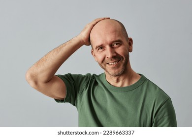 Portrait of mature bald man smiling at camera and posing confidently with hand on head, copy space