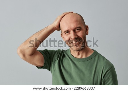 Portrait of mature bald man smiling at camera and posing confidently with hand on head, copy space