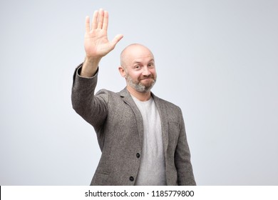 Portrait Of A Mature Bald Man In Suit Wave Hand Welcome. Human Emotion Expression And Lifestyle Concept. Studio Shoot