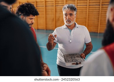 Portrait of a mature basketball coach and his diverse team having a team talk while gathered together at the court and cheering each other. Disusing game tactic during a match or a practice. - Powered by Shutterstock