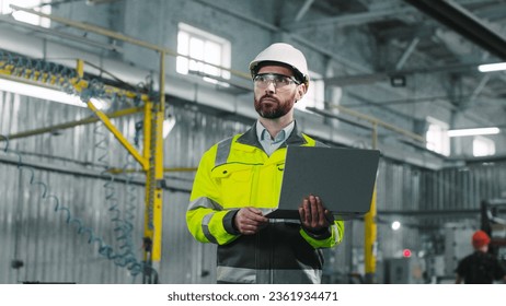 Portrait of mature bearded male engineer. Industrial manufactory worker is standing and holding laptop at construction. Architect dressed up in protective clothes and helmet inspecting work process. - Powered by Shutterstock