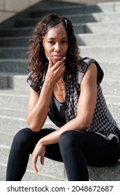 Portrait Of Mature Black Woman Sitting On Stairs. She Has Curly Hair.