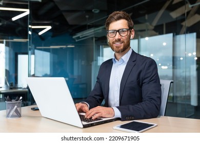 Portrait of mature boss inside office with laptop, successful and satisfied investor manager looking at camera and smiling man in glasses and business suit, investor with beard sitting on chair. - Shutterstock ID 2209671905