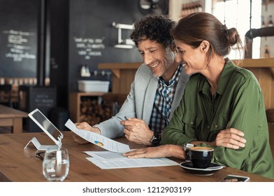 Portrait of mature business man and casual businesswoman sitting in cafe and discussing sales graph. Group of two middle aged coworkers working comparing forecasting graphics. Happy businesspeople. - Powered by Shutterstock