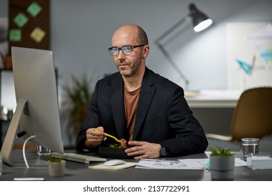 Portrait Of Mature Businessman Eating Takeout Dinner At Workplace While Working Late At Night In Office, Copy Space
