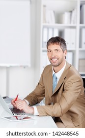 Portrait Of Mature Businessman With Laptop At Office Desk