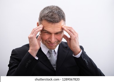 Portrait Of Mature Businessman Suffering From Headache Against White Background