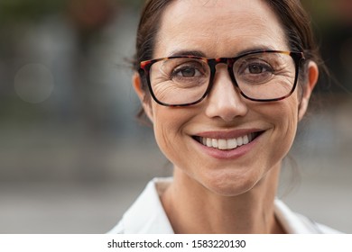 Portrait Of Mature Businesswoman Wearing Eyeglasses And Looking At Camera. Close Up Face Of Cheerful Woman With Spectacles Smiling Outdoor. Confident Beautiful Entrepreneur Wearing Specs.