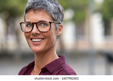 Portrait of mature businesswoman wearing eyeglasses while looking at camera. Smiling middle aged lady with grey hair standing outdoor. Close up face of happy successful woman with glasses, copy space.