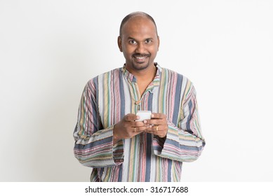 Portrait Of Mature Casual Business Indian Man Using Smartphone And Smiling, Mobile Apps Concept, Standing On Plain Background With Shadow.