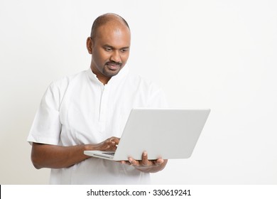 Portrait Of Mature Casual Business Indian Man Using Laptop Computer, Standing On Plain Background With Shadow.