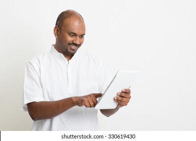 Portrait Of Mature Casual Business Indian Man Using Digital Tablet Pc, Standing On Plain Background With Shadow.