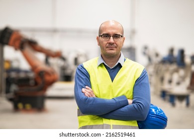 Portrait Of Mature Caucasian Engineer Worker Is Standing Confidently In Blue Work Dress And Safety Helmet In Front Of Hi-tech Industry Factory.