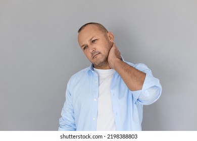 Portrait of mature Caucasian man rubbing his neck. Balding guy wearing white T-shirt and blue shirt suffering from neck ache. Aging disease concept - Shutterstock ID 2198388803