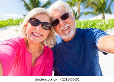 Portrait Of Mature Caucasian Senior Couple In Bright Clothing Carefree Outdoors In Sunglasses On Tropical Luxury Beach Resort 