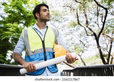 Portrait Mature Construction Engineer Confident With Blueprint For Plan Project And Statistical Report On Site Middle Cityscape Near Public Park. Back View Of House Property With Laborer.