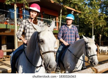 Portrait Of Mature Couple In Helmets Riding By Horse At Barn At Summer Day