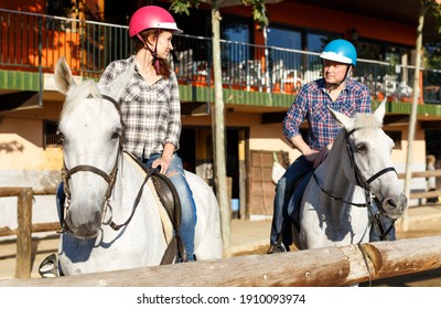 Portrait Of Mature Couple In Helmets Riding By Horse At Barn At Summer Day