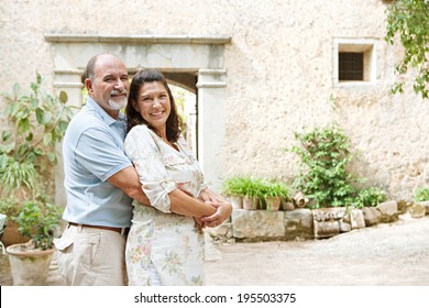 Portrait Of A Mature Couple Together In A Luxury Home Garden On Holiday And Hugging Looking At Camera, Relaxing On A Summer Vacation. Healthy Senior People Enjoying Retirement, Outdoors Lifestyle.