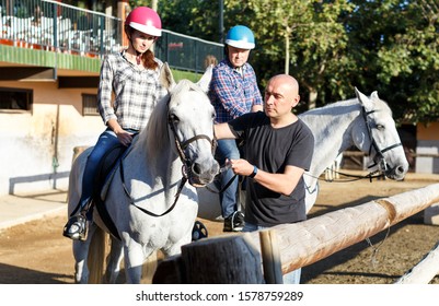Portrait Of Mature Couple With Trainer Riding Horse At Farm Outdoor
